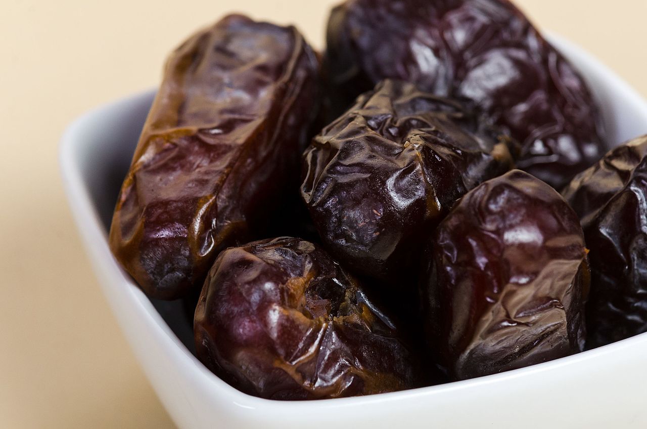 Medjool dates in a white bowl on a cream ground
